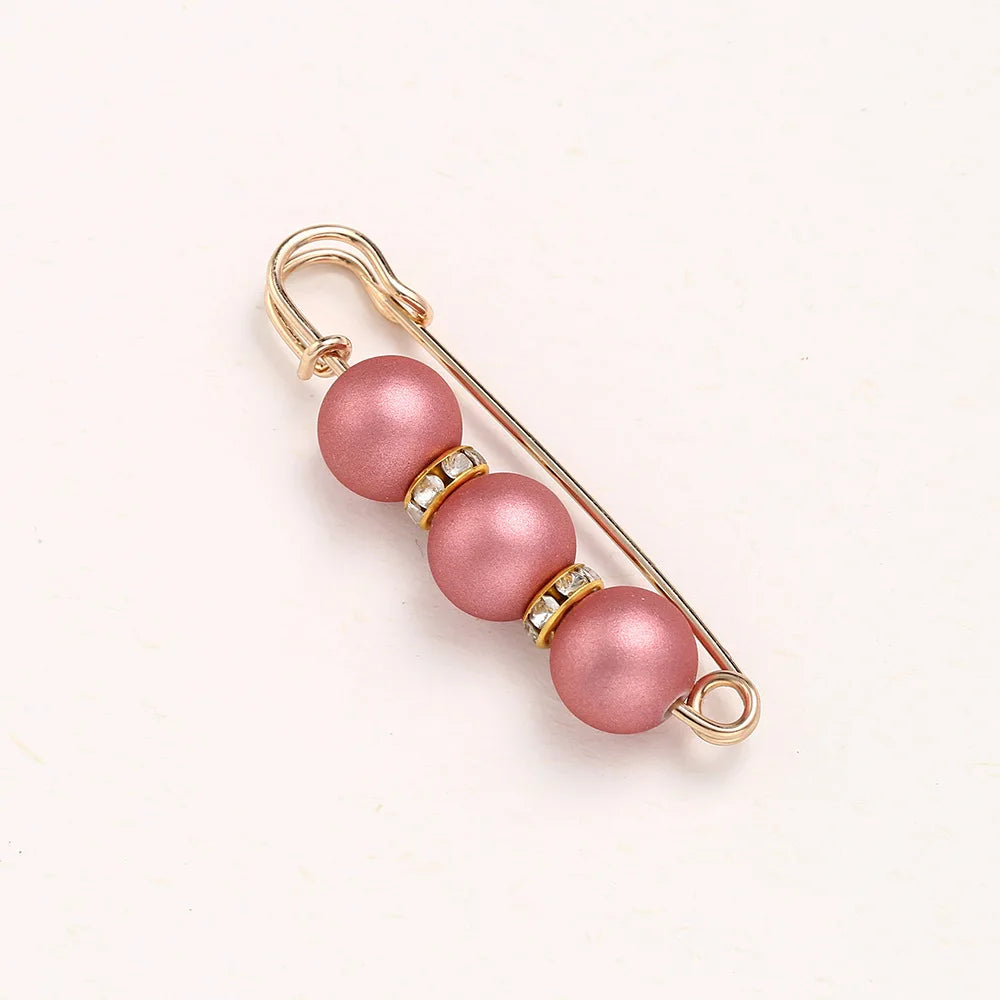 A delicate gold-toned adjustable pearl brooch featuring three round pink pearls.