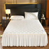 White quilted bed skirt with vertical pleats covering a queen mattress.
