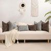 A sofa decorated with various textured gray and brown chenille throw pillow covers and a cream blanket.