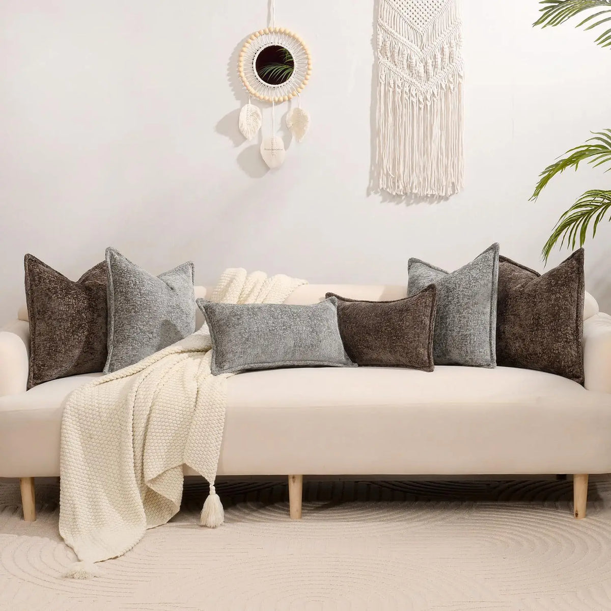 A sofa decorated with various textured gray and brown chenille throw pillow covers and a cream blanket.