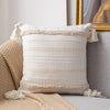 A cream woven throw pillow cover with beige stripes and tassels resting on a gray sofa.