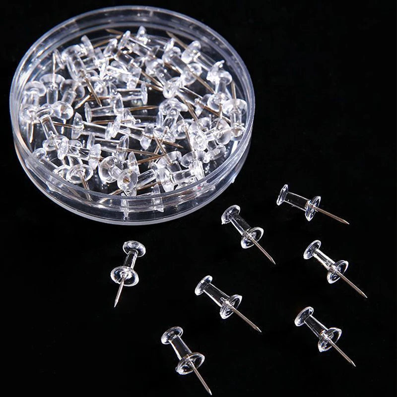 A clear plastic container filled with numerous push pins featuring steel tips.