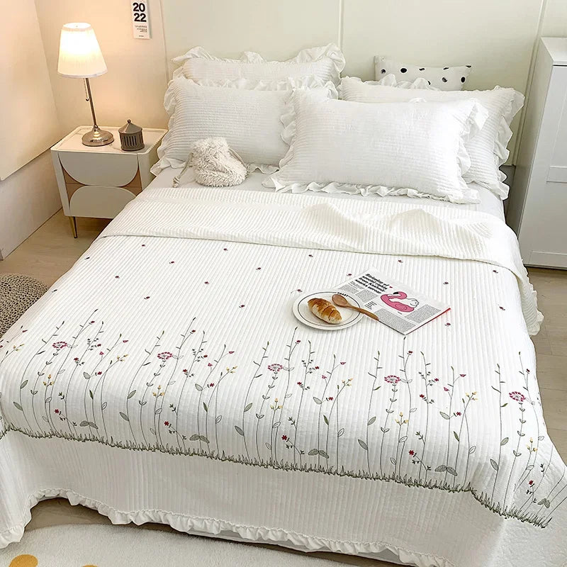 White quilt bedspread set with floral embroidery and white pillows on a bed.