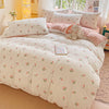 A pink floral printed bedding set featuring white sheets and pillows with a stuffed rabbit toy.