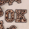 Iron-on patches of the letter O and K in leopard print on a light fabric background