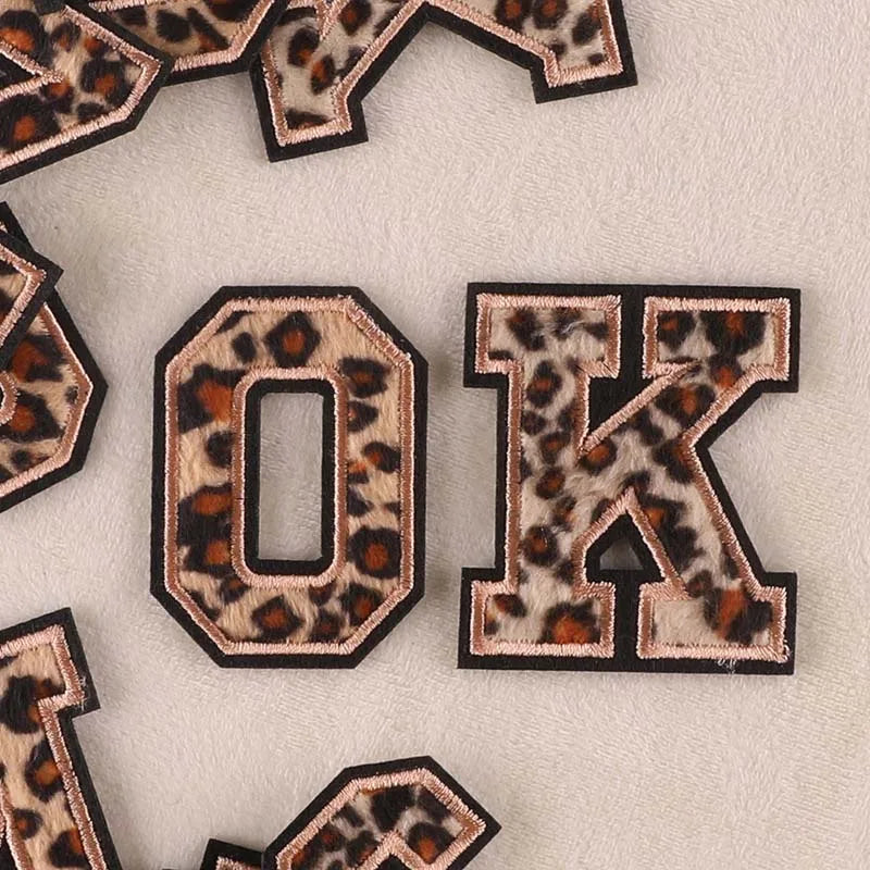 Iron-on patches of the letter O and K in leopard print on a light fabric background