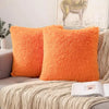 Two bright orange faux fur throw pillows resting on a beige knitted blanket.