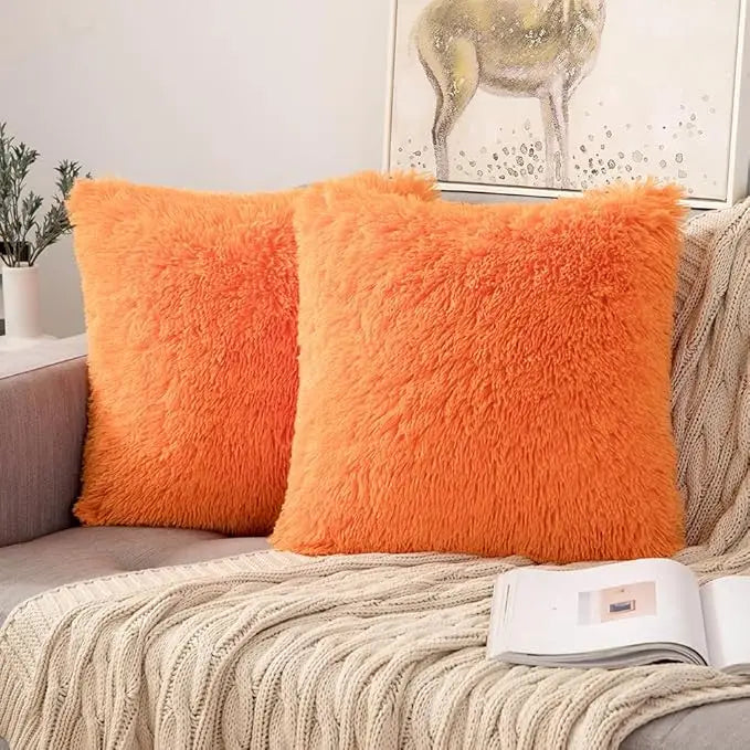 Two bright orange faux fur throw pillows resting on a beige knitted blanket.