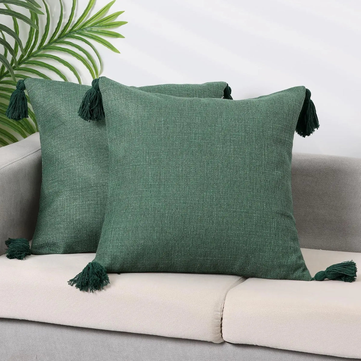 A dark olive green linen throw pillow resting on a light sofa with green foliage in the background.