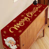 A festive red table runner with gold lettering and a Santa face design displayed on a wooden cabinet.