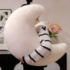 A close-up of a white, sheepskin-like moon shaped throw pillow with black striped sleeves.