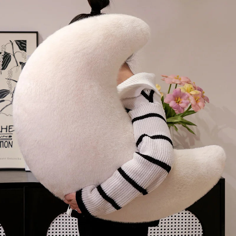 A close-up of a white, sheepskin-like moon shaped throw pillow with black striped sleeves.