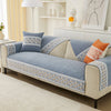 A blue and beige quilted sofa cover with lace trim and decorative pillows displayed on a modern sofa.