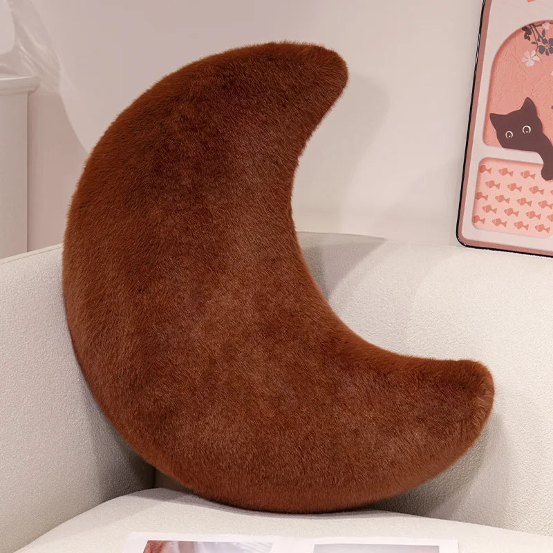 A brown moon-shaped throw pillow resting on a white surface.