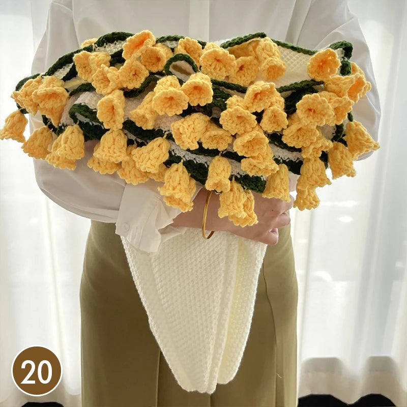 A hand knitted floral rose bouquet throw blanket in yellow and green is held by a person wearing a white shirt and beige pant