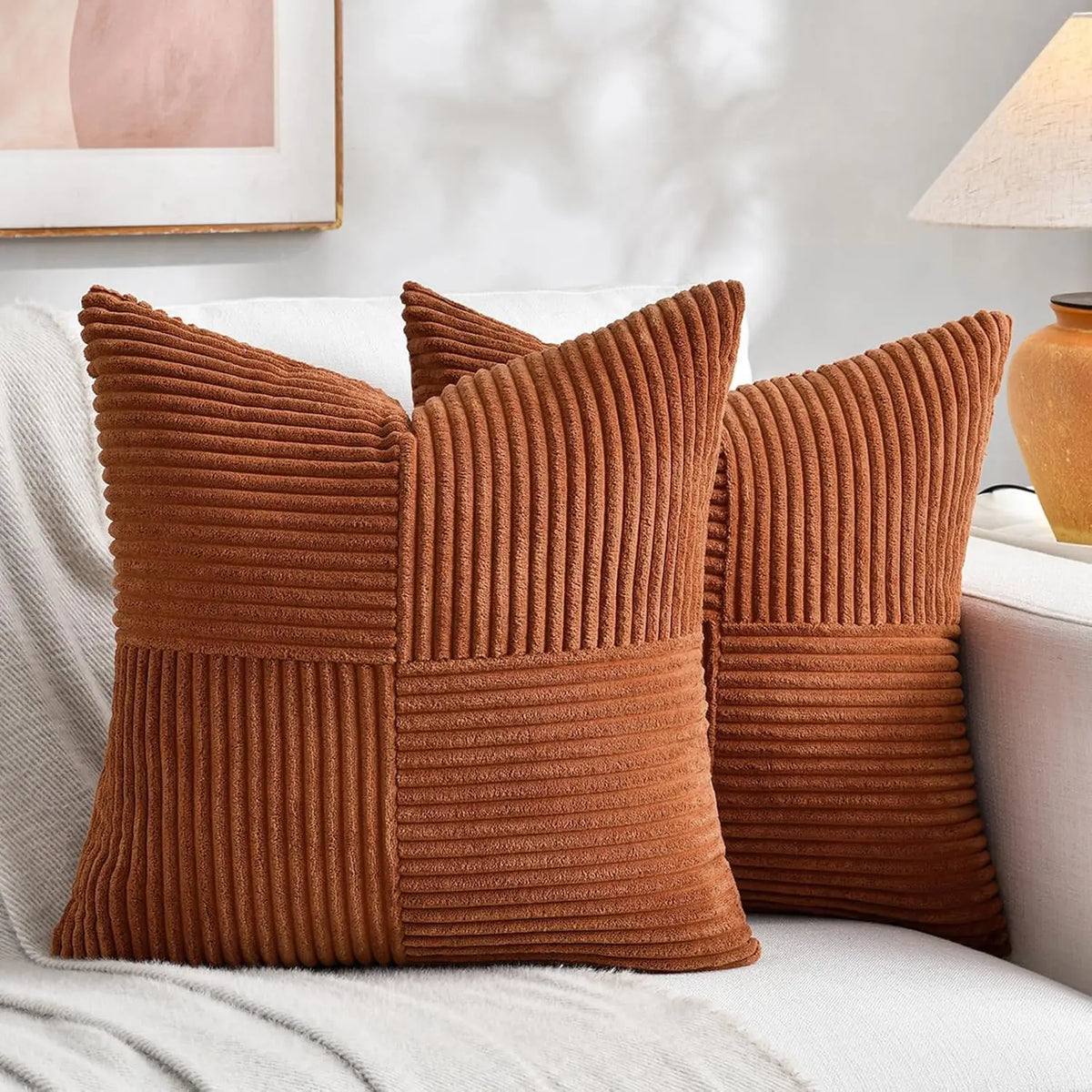 A set of four brown corduroy throw pillow covers with a vertical ribbed texture and patchwork design resting on a white sofa.