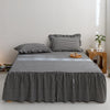 A black and white plaid cotton bed skirt cover draped over a bed, with pillows and a wooden side table nearby.