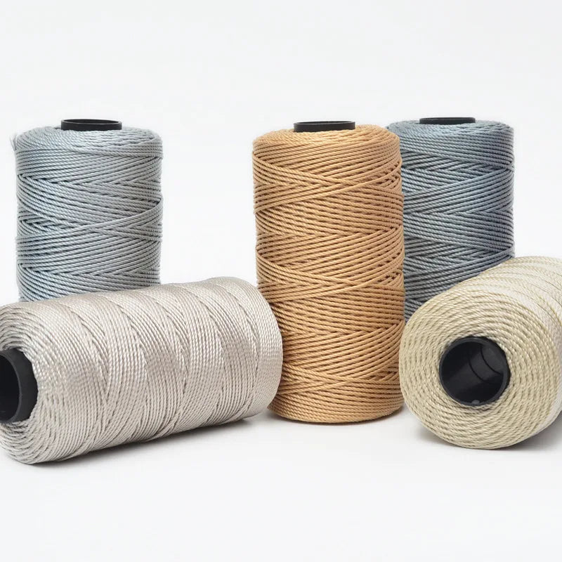 Four spools of hand knitting and crochet cord in various shades of gray and beige yarn