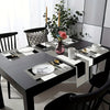 A modern geometric placemat set is displayed on a dark dining table with white plates and gold cutlery, accented by a green p
