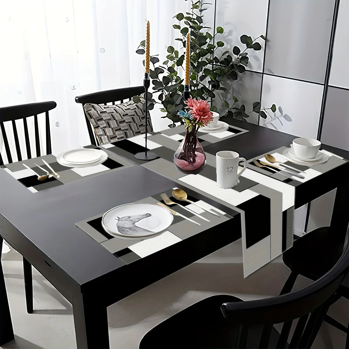 A modern geometric placemat set is displayed on a dark dining table with white plates and gold cutlery, accented by a green p