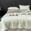 A light mint green lightweight cooling blanket is draped over a bed, with a white candle and small decorative items on top.