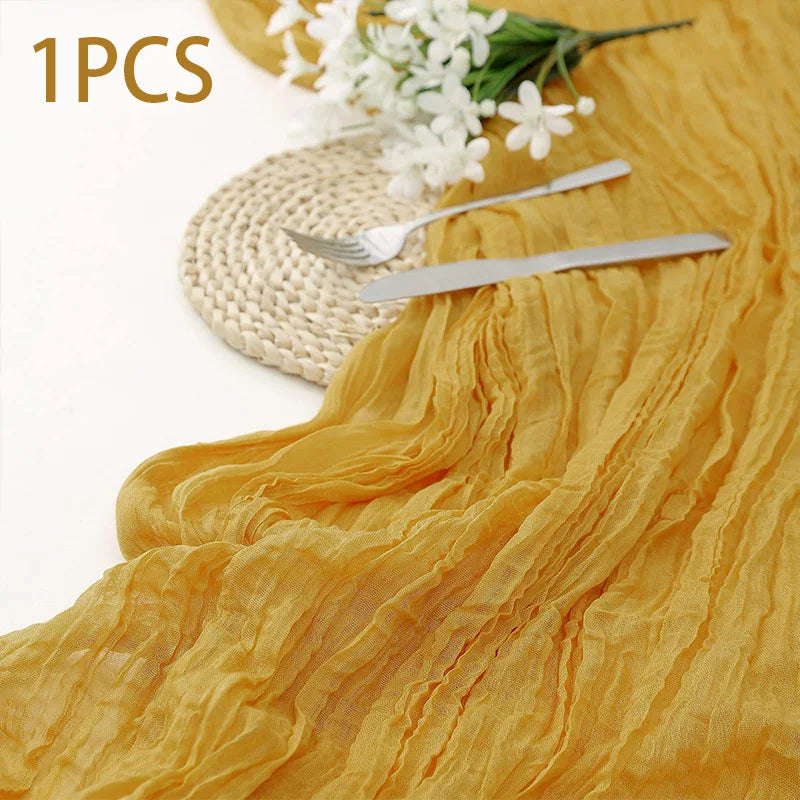 A golden yellow semi-sheer gauze table runner draped with a white floral arrangement and silver cutlery.