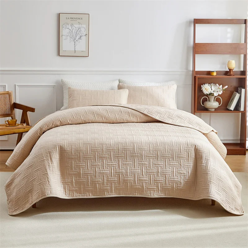 A beige quilted cotton bedspread set with matching pillows on a bed in a bright room.