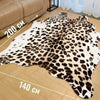 A white and brown leopard print faux animal skin rug laid out on a wooden floor.