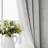 A white ceramic vase holds a bouquet of white and green flowers next to a gray linen curtain.