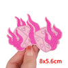 Pink embroidered iron-on patches shaped like flames and hearts being held by a hand