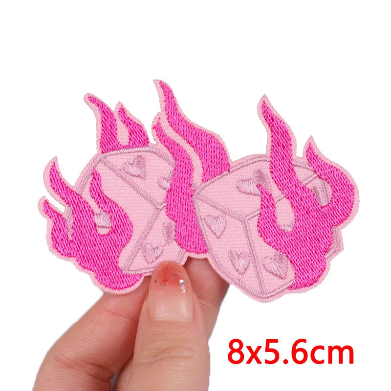 Pink embroidered iron-on patches shaped like flames and hearts being held by a hand