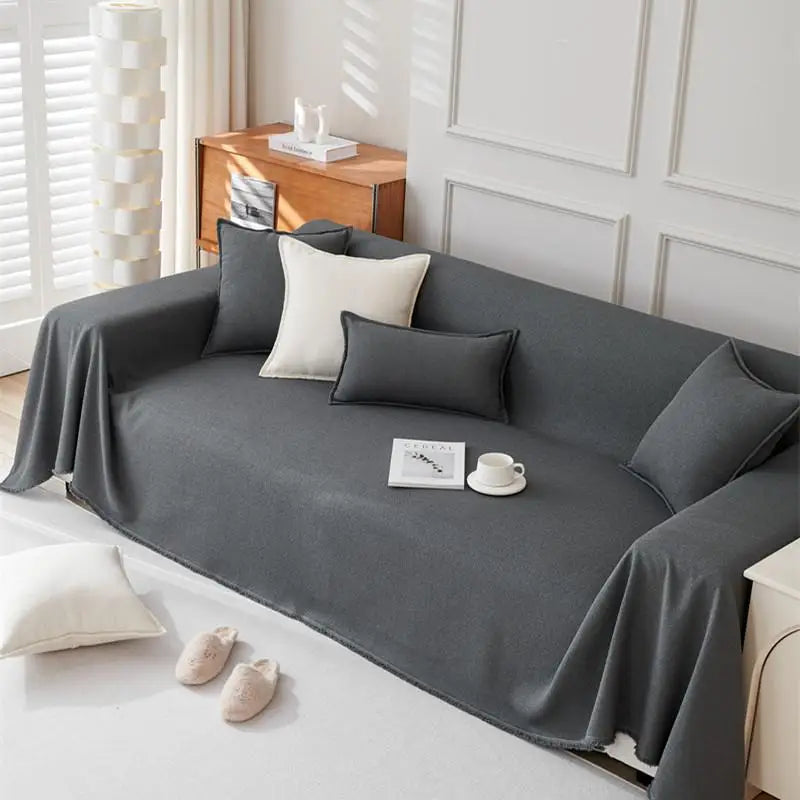 A charcoal gray anti-scratch sofa cover draped over a sofa with white and dark accent pillows.