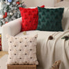 Three festive throw pillows in red, dark green, and cream are displayed on a light-colored sofa.