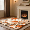 A beige flannel throw blanket featuring an orange pumpkin and autumn leaf pattern displayed on a wooden floor.