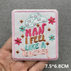 Pink embroidered patch with the slogan MAN I FEEL LIKE A TEACHER in pink and teal thread on a light gray fabric background