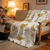 A beige plush throw blanket featuring a pattern of C-Curious George characters on a light sofa.