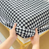 Hands are pulling up a black and white checkered flannel fitted sheet with deep pockets.