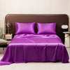 A luxurious purple satin flat bed sheet set with two pillows is displayed on a bed against a brown headboard.