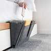 A felt bedside storage organizer with a hanging pocket is shown on a white nightstand next to a bed.