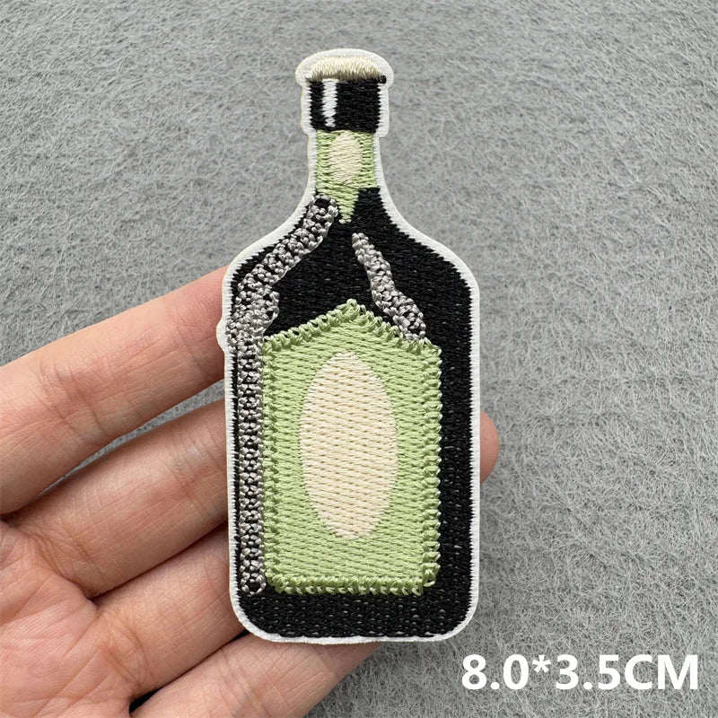 An embroidered iron-on patch shaped like a glass bottle with a green liquid and black and white detailing.
