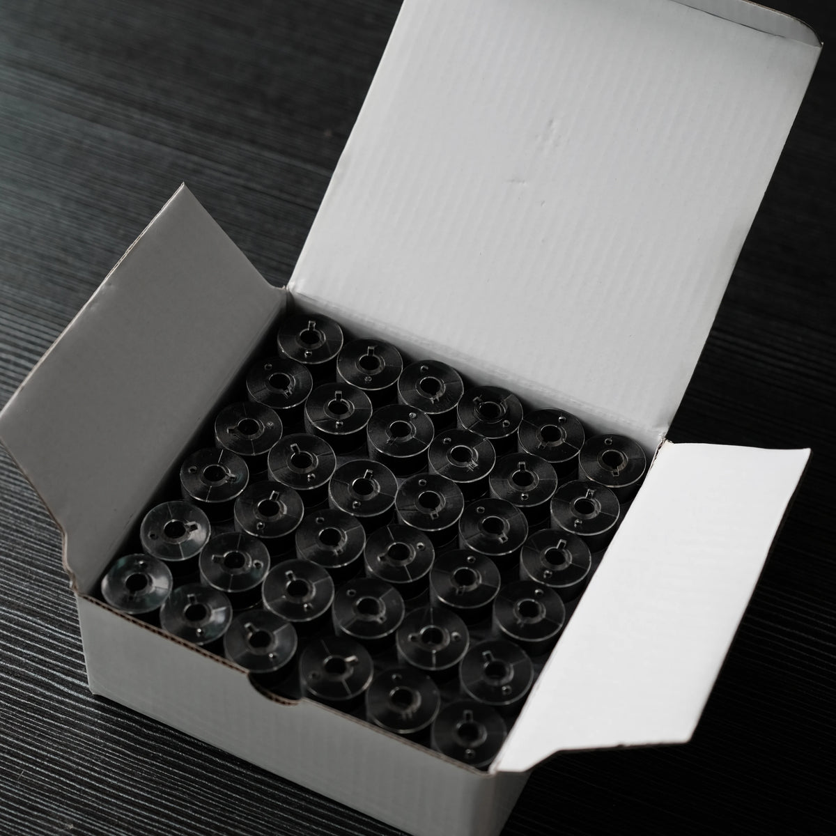 A white box containing 144 small, clear embroidery bobbin threads arranged in a grid.