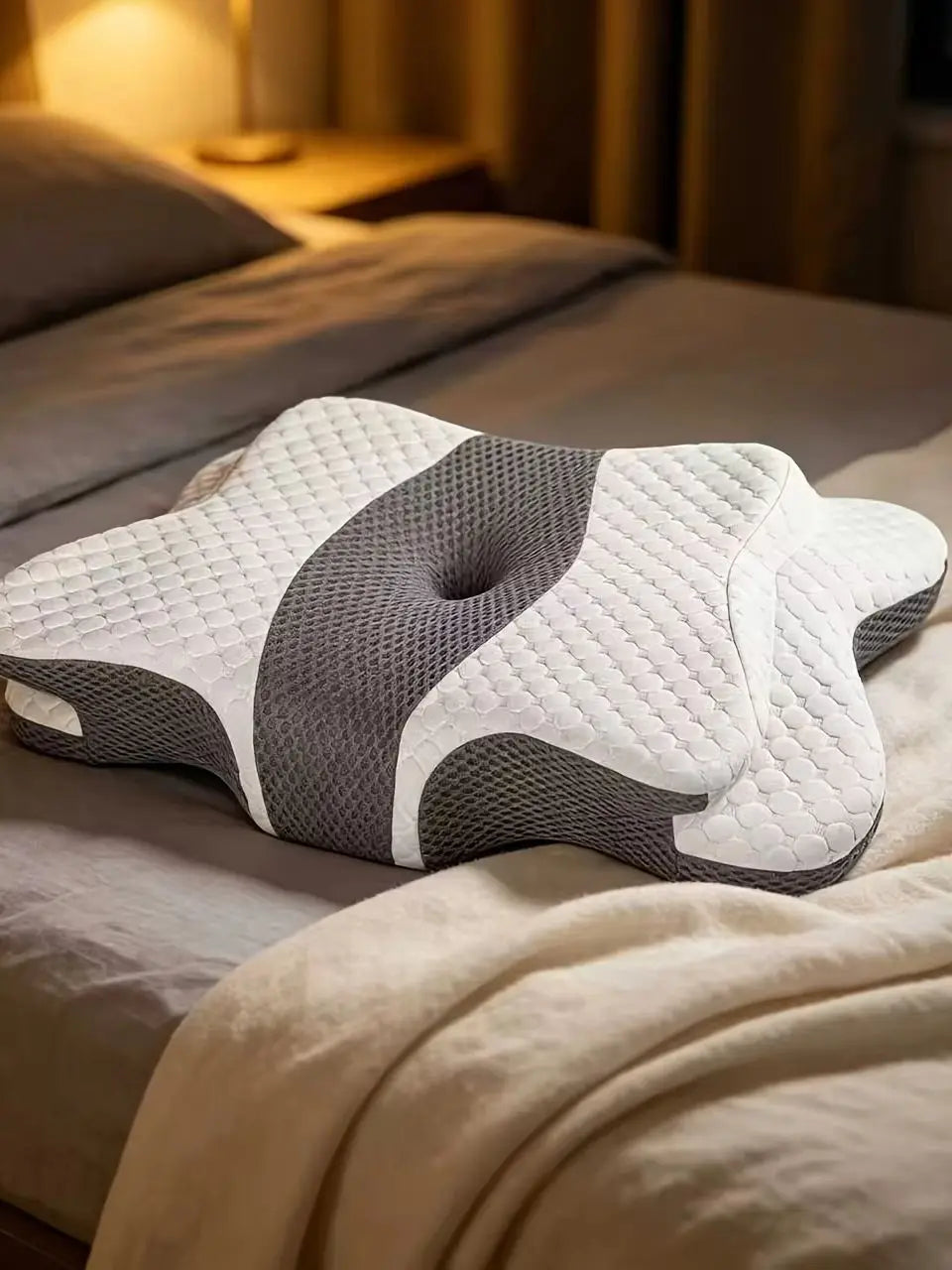 A white and gray ergonomic memory foam neck pillow resting on a bed with soft bedding.