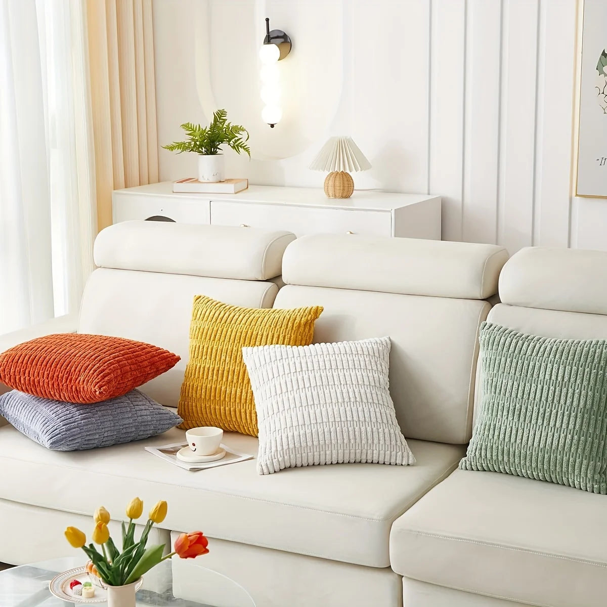 A collection of decorative throw pillows in orange, yellow, white, and green are displayed on a white sofa.