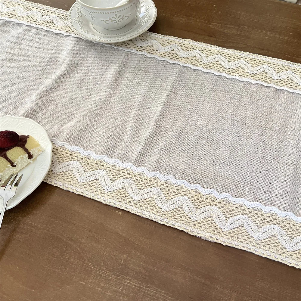 A beige crochet macrame lace table runner with white edging and a teacup on a wooden table.