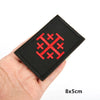 Black fabric patch embroidered with a red military cross shield design being held in a hand.