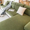 A sectional sofa upholstered in olive green fabric with a striped throw blanket and a cream cushion.