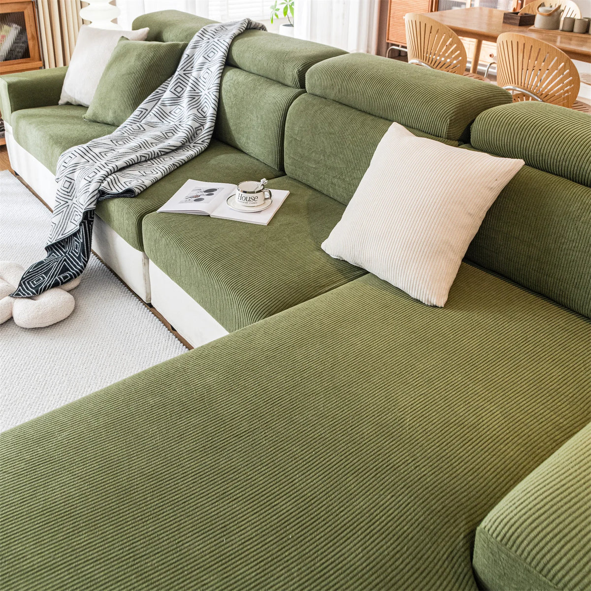 A sectional sofa upholstered in olive green fabric with a striped throw blanket and a cream cushion.