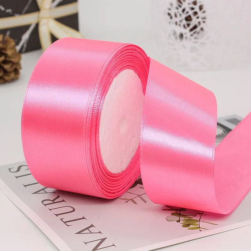 Roll of bright pink satin craft ribbon shown on a white surface.