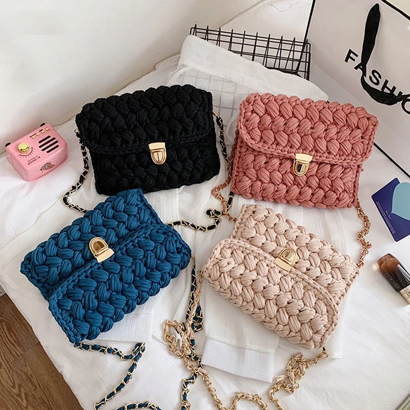 A collection of five textured fabric bags in black, pink, blue, and beige with gold metal clasps displayed on white fabric.