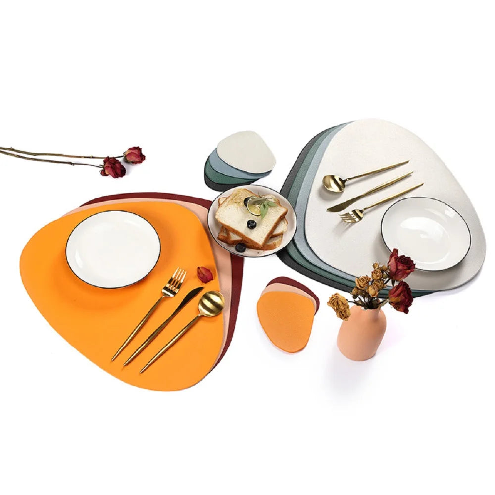 A set of reusable vinyl placemats and tableware including plates, cutlery, and a small vase with dried flowers.